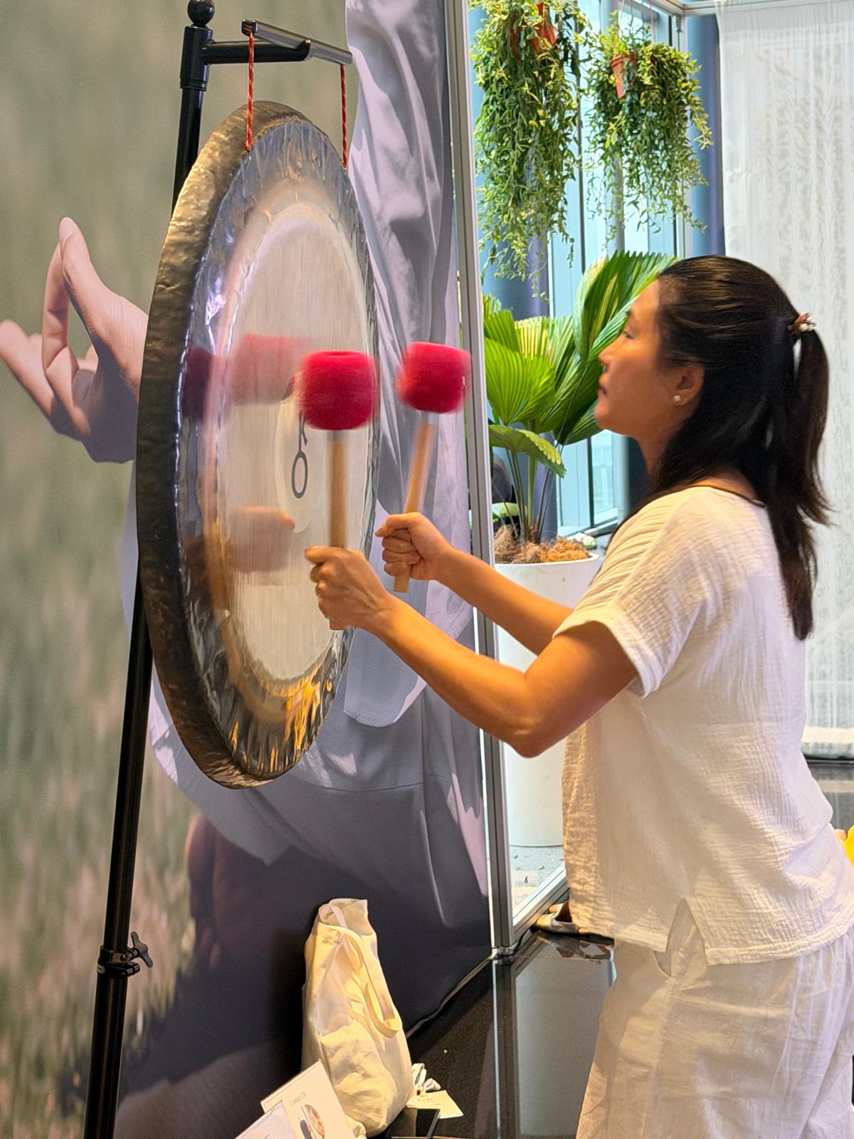 Jacqui playing a large Gong with two mallets during a corporate Sound Bath